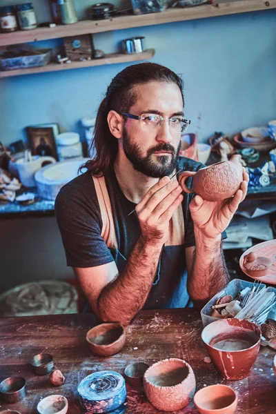Pensive Potter w okularach w jego własnym warsztacie jest robocza na nowym czajniczek ręcznie. — Zdjęcie stockowe