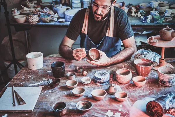 Pembuat tembikar besar berkacamata di bengkelnya sendiri bekerja pada teko baru buatan tangan . — Stok Foto