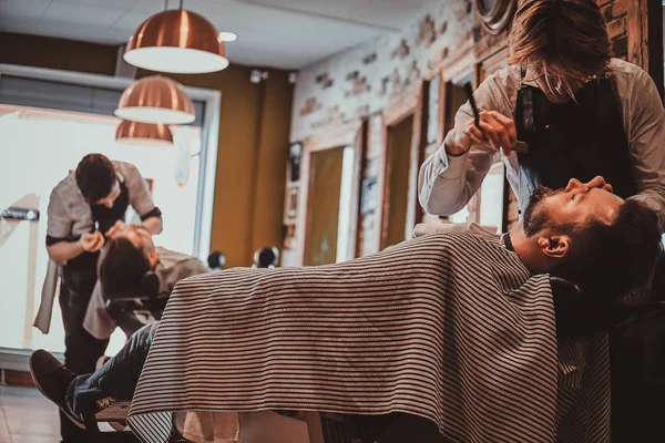 現代の理髪店でその後の美容師は、クライアントのヘアカットに取り組んでいます. — ストック写真