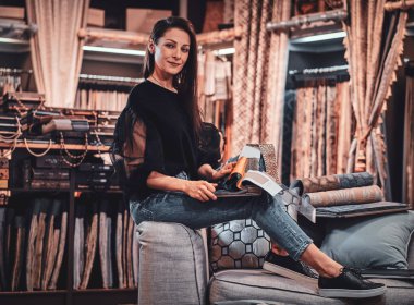 Modern tasarımcı, giysilerle çevrili işyerinde kanepede oturuyor..