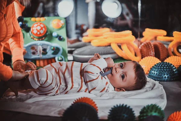 Happy smiling cute baby is lying on the special table surrounded by ortopedic toys — Stock Photo, Image