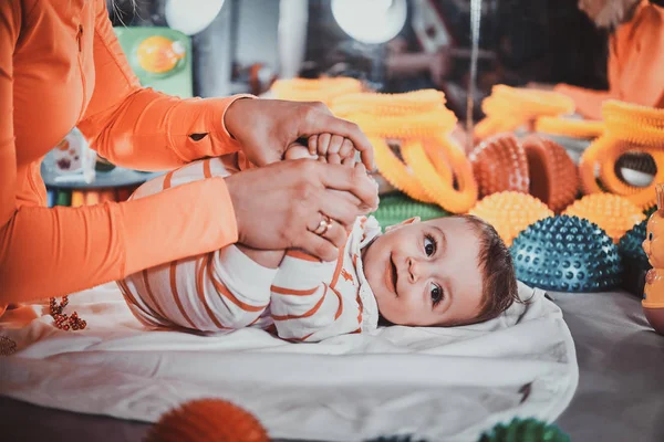 Feliz sorrindo bebê bonito está deitado na mesa especial cercado por brinquedos ortopédicos — Fotografia de Stock