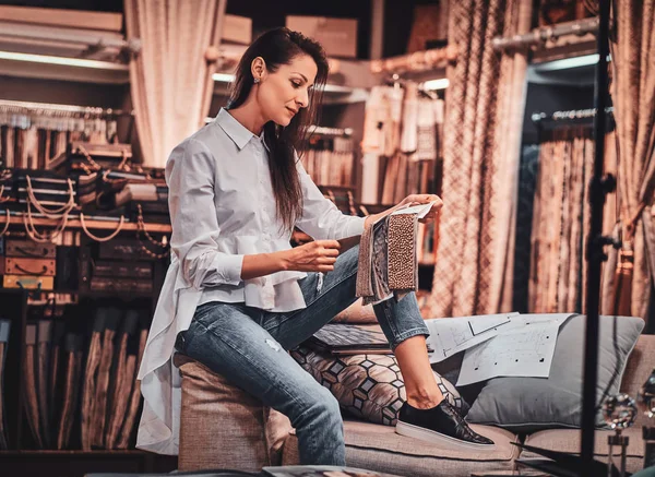 Ijverige getalenteerde vrouw zit op de Bank in haar kleding Studio met tekeningen — Stockfoto