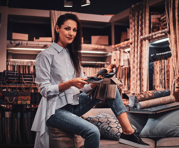 Веселая женщина сидит на диване в своей текстильной мастерской
