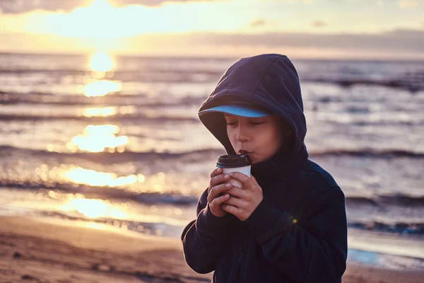 小さな男の子は、日没時に、海辺でお茶を飲んでいます — ストック写真