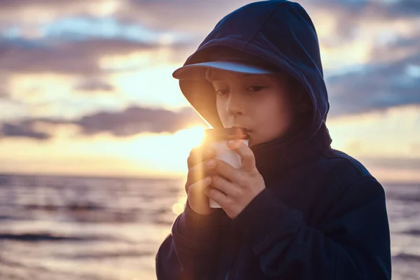 小さな男の子は、日没時に、海辺でお茶を飲んでいます — ストック写真