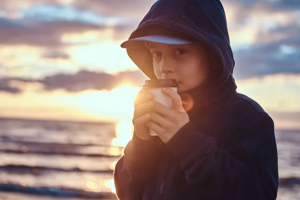 Küçük çocuk gün batımında deniz kenarında çay içiyor. — Stok fotoğraf
