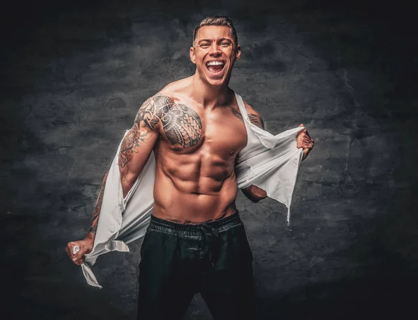 Atlético masculino com uma tatuagem em seu peito rasgando t-shirt . — Fotografia de Stock