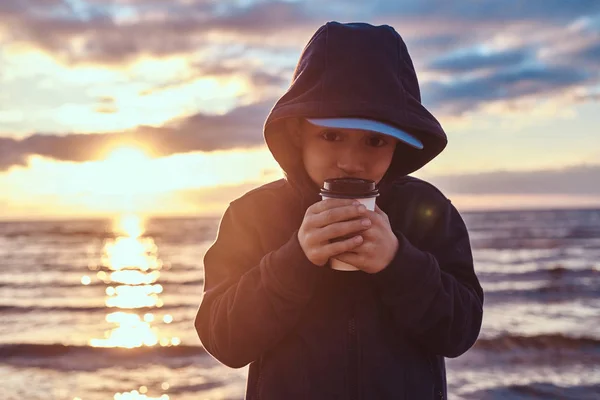 Kleiner Junge trinkt Tee am Meer, bei Sonnenuntergang — Stockfoto