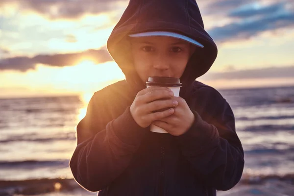 小さな男の子は、日没時に、海辺でお茶を飲んでいます — ストック写真