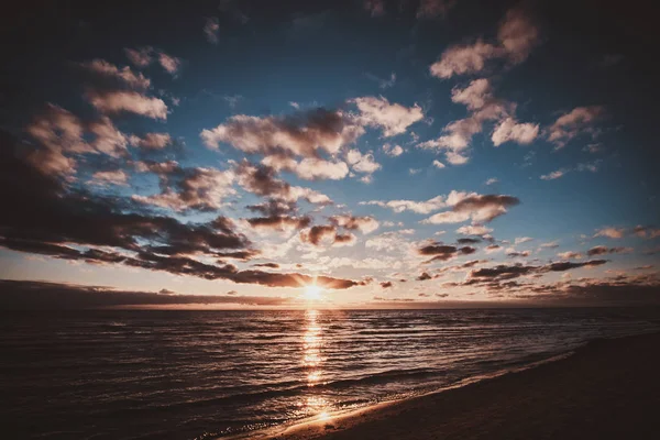 Cênico pôr-do-sol colorido à beira-mar com pequenas nuvens — Fotografia de Stock