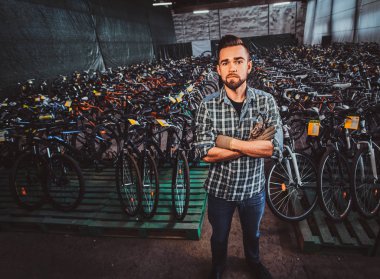 Genç ve çekici bir adam fotoğrafçı için bisiklet depolarında poz veriyor..