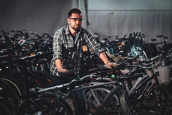 Nice hardworking man is working with bicycles at warehouse.