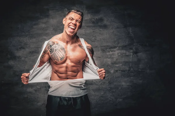 A man with tattoo ripping t shirt on his chest.