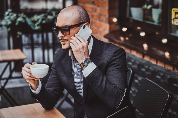 Allvarlig framgångsrik man ringer med mobilen och njuter av sitt kaffe. — Stockfoto