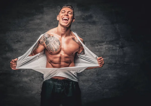 Un hombre con tatuaje rasgando camiseta en el pecho . — Foto de Stock