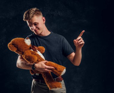 Mutlu gülümseyen adam peluş ayısına bir şeyler gösteriyor.