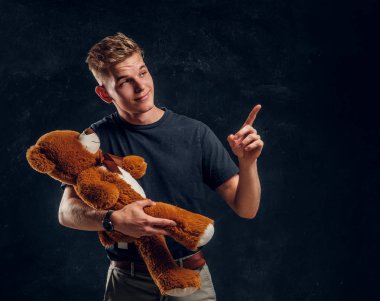 Mutlu gülümseyen adam peluş ayısına bir şeyler gösteriyor.