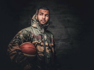 Siyah bir erkek basket topu tutar.