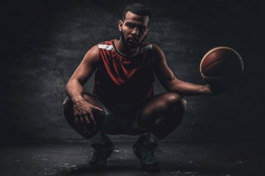 Siyah bir basketbolcu bir yere oturur ve sepet topu tutar.