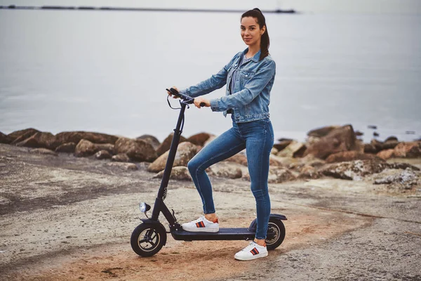 Sporty woman is riding electro scooter by seaside