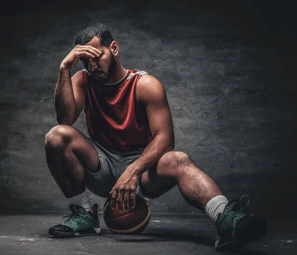 O jogador de basquete senta-se em um soalho e mantém uma bola . — Fotografia de Stock