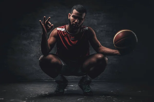 Ein schwarzer Basketballspieler sitzt auf dem Boden und hält einen Basketballkorb. — Stockfoto