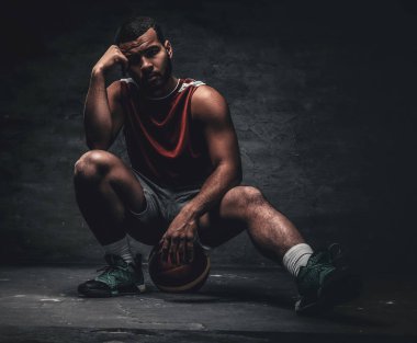 Siyah bir basketbolcu bir yere oturur ve sepet topu tutar.