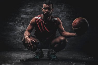 Siyah bir basketbolcu bir yere oturur ve sepet topu tutar.