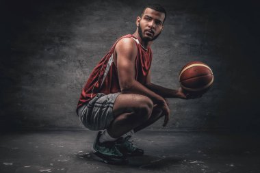 Siyah bir basketbolcu bir yere oturur ve sepet topu tutar.