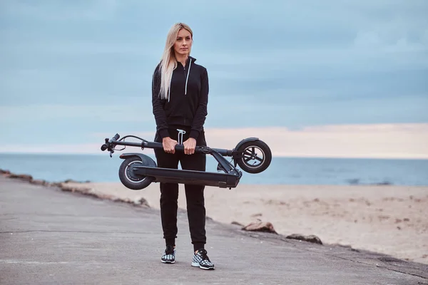 Mujer en ropa deportiva está sosteniendo plegado electro scooter —  Fotos de Stock