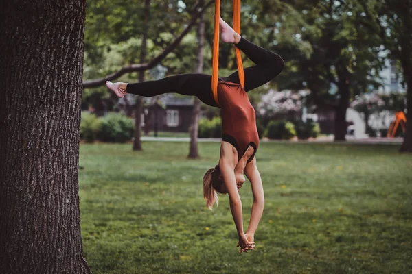 Jong aantrekkelijk meisje met lang haar doet oefeningen op sling in het park. — Stockfoto