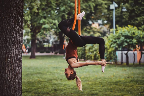 Jong aantrekkelijk meisje met lang haar doet oefeningen op sling in het park. — Stockfoto