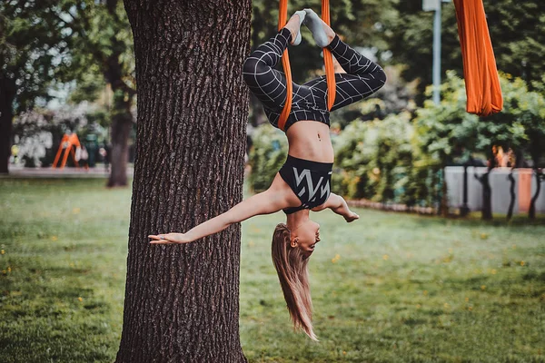 Junges attraktives Mädchen mit langen Haaren macht im Park Übungen auf dem Sling. — Stockfoto