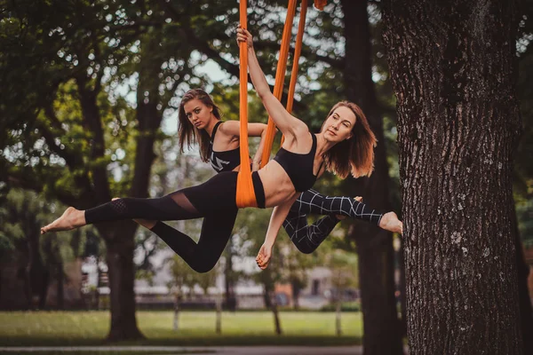 Duas belas garotas graciosas estão fazendo exercícios de alongamento nas fundas — Fotografia de Stock