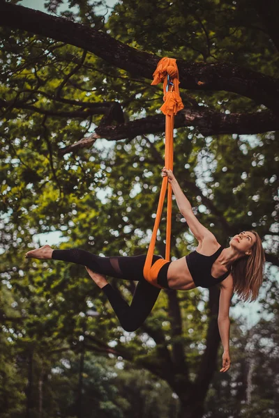 Attraktives Mädchen mit langen Haaren macht im Wald Übungen auf einer Schlinge. — Stockfoto