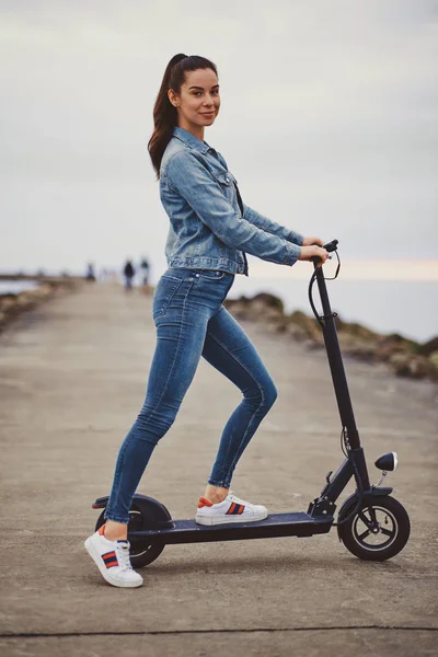 Mulher desportiva está montando electro scooter à beira-mar — Fotografia de Stock