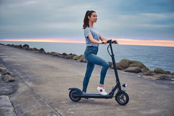 Sportowa kobieta jeździ Electro Scooter przez wybrzeże — Zdjęcie stockowe