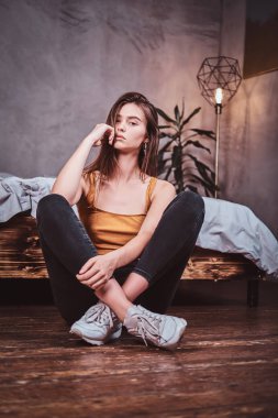 Young woman in sheakers is sitting on the floor
