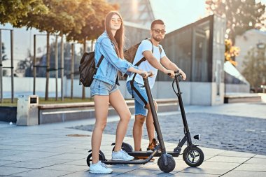 Genç çift, elektro scooterların keyfini çıkarıyor.