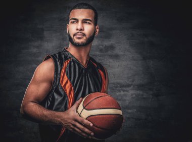 Basketbolcu gri arka plan üzerinde bir top tutar.