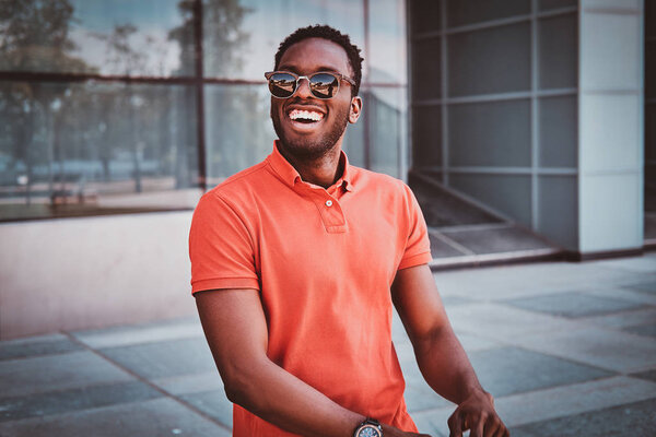 Portrait of happy smiling afro student in sunglasses over glass building.