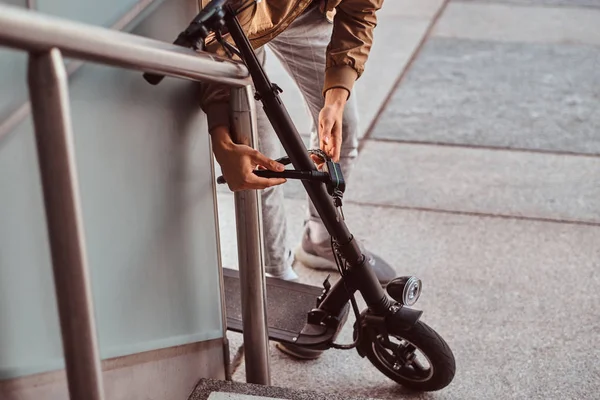 El hombre está aparcando su electro scooter y cerradura de cadena ut en él —  Fotos de Stock