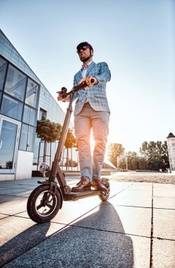 Adam büyük cam binanın yakınında onun yeni elektro scooter sürüyor