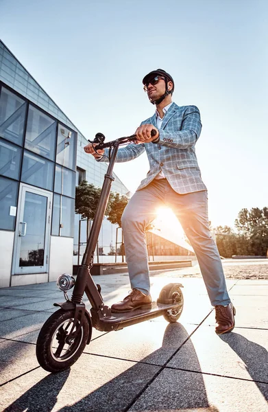 Manusia mengendarai skuter elektro barunya di dekat bangunan kaca besar. — Stok Foto