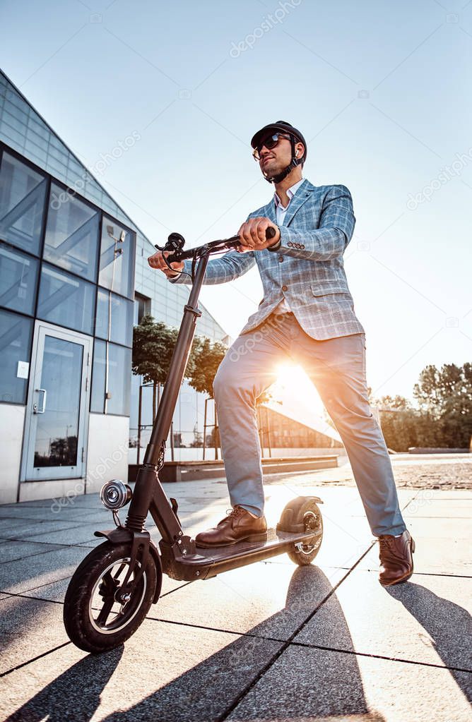 Man is driving his new electro scooter near big glass building