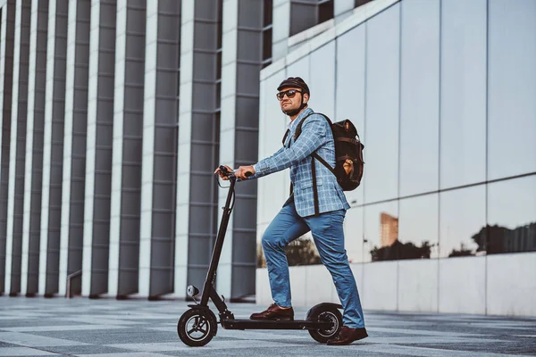 Manusia mengendarai skuter elektro barunya di dekat bangunan kaca besar. — Stok Foto