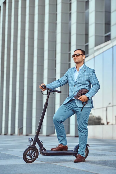 Mann fährt mit seinem neuen Elektroroller in der Nähe eines großen Glasbaus — Stockfoto