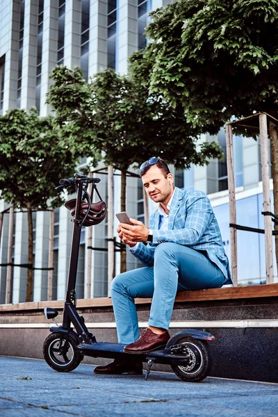 Красивий чоловік розслабляється на лавці з скутером і смартфоном — стокове фото