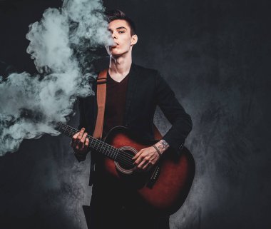 Çekici adam akustik gitar çalıyor ve sigara içiyor